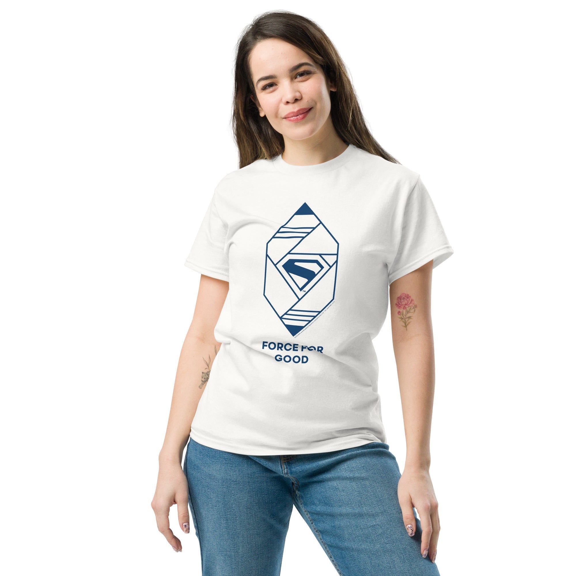 Femme souriante portant un t-shirt blanc Force for Good avec logo Superman 2025 en bleu, design géométrique moderne et stylé.