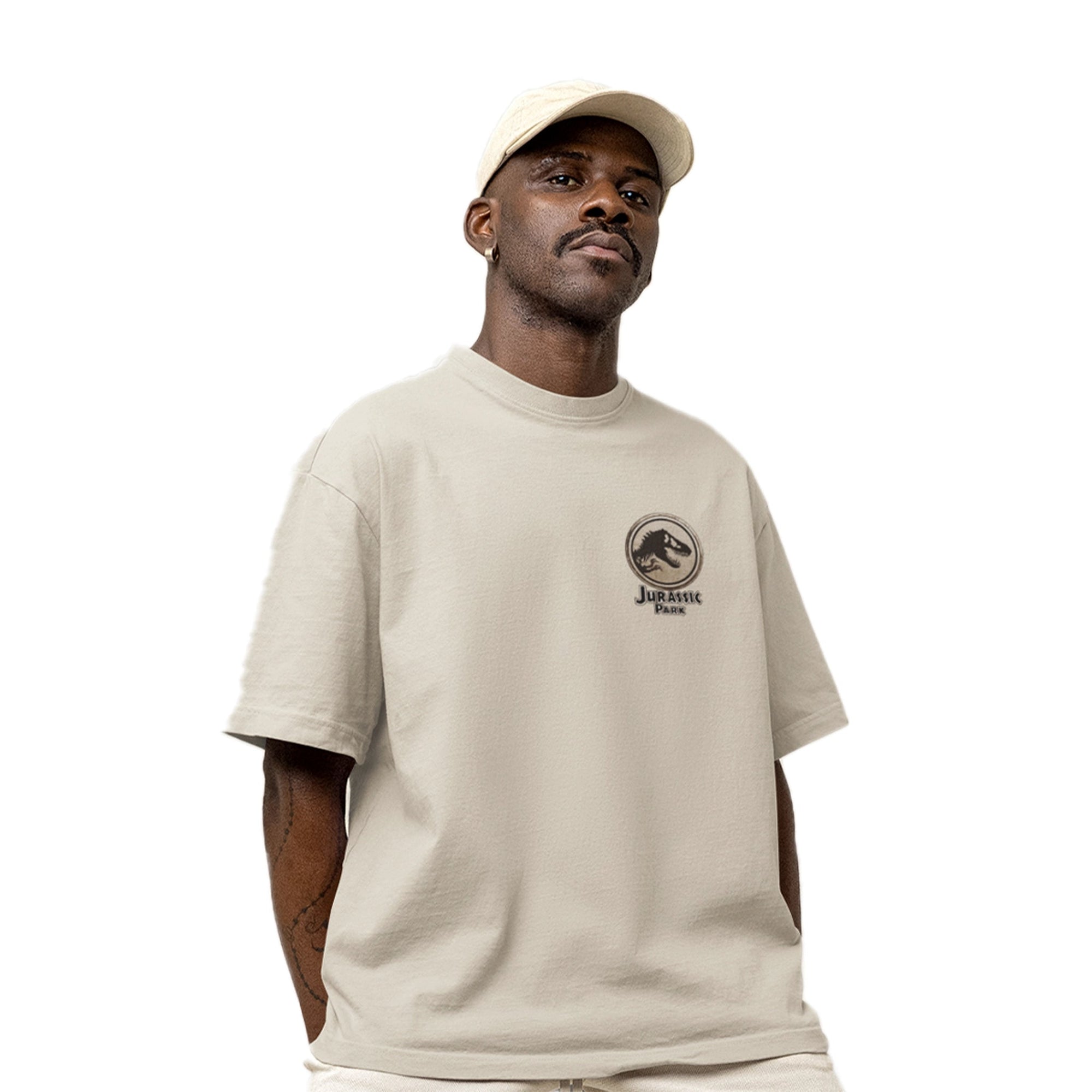 T-shirt oversize beige Jurassic Park avec logo Jurassic en noir sur la poitrine, porté par un homme pour un look streetwear tendance.